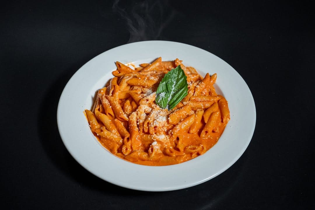 Penne alla vodka in a white bowl on a wooden table, from a Bravo Pizza Instagram post
