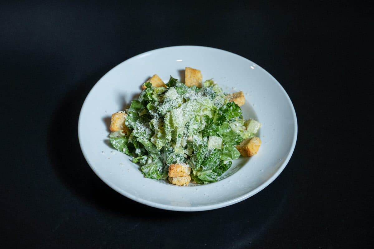 Caesar salad with croutons and shaved cheese in a black bowl